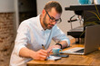 © Jake Jakab/ADDICTIVE STOCK - Focused male barista sitting at wooden counter with laptop and taking notes in notebook while working in coffee shop