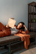 © Jordi Bataller/ADDICTIVE STOCK - Relaxed positive young ethnic Indian female in stylish outfit lying on wooden bench and reading old book while resting in room with minimalist interior