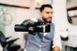 © Jake Jakab/ADDICTIVE STOCK - Masculine male hairdresser in glove demonstrating professional electric clipper in barbershop on blurred background