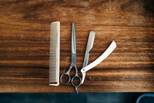 Top View Of Scissor And Comb Near Straight Razor With Sharp Metal Blades On Wooden Table In Hairdressing Salon