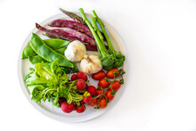 Top View Of Fresh Green Beans Garlic Cherry Tomatoes On Branch With Radish And Greens On Plate Above White Background
