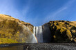 © Josu Torrealday/ADDICTIVE STOCK - Unrecognizable traveler standing near amazing waterfall and rainbow in mountains during vacation in Iceland