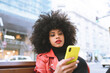 © Jose Carlos Cerdeno/ADDICTIVE STOCK - Stylish astonished African American female reading news on cellphone sitting on bench in city