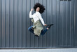 © Jose Carlos Cerdeno/ADDICTIVE STOCK - Side view of happy young African American woman with curly hair in trendy outfit smiling and looking at camera while jumping on street