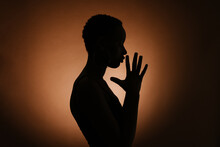 Silhouette Of Anonymous Ethnic Female Clasping Hands And Praying Against Brown Background