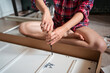 © Juan Alberto Ruiz/ADDICTIVE STOCK - Crop faceless female sitting on floor and screwing screws in wooden board while assembling new furniture at home