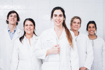 A group of five doctors in white coats stand in a hospital room smiling while one of them has a report in his hands
