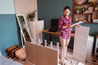 © Juan Alberto Ruiz/ADDICTIVE STOCK - High angle of busy Asian female in domestic clothes standing with instruction and assembling furniture in new flat
