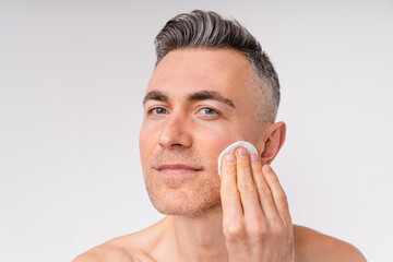 Attractive middle-aged man using cotton pad shirtless isolated over white background