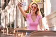 © Manuel Ruiz/ADDICTIVE STOCK - Cheerful teenage woman taking selfie while sitting at table in street cafe in Madrid