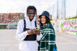 © Luis Manuel Munoz/ADDICTIVE STOCK - Young content multiracial partners in stylish apparel sharing cellphone on urban pavement in sunlight