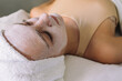© Marina Gallardo/ADDICTIVE STOCK - High angle of young calm female client with towel on head lying on couch with closed eyes and white facial mask and relaxing during skincare procedure