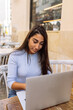 © Marina Gallardo/ADDICTIVE STOCK - Young ethnic female freelancer sitting at table and working on remote project on laptop while spending time in outdoor cafe