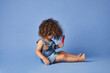 © MATHIAS ALVEZ/ADDICTIVE STOCK - Full body side view of upset little girl on summer clothes barefooted sitting with ice cream against studio blue background