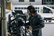 © Oscar Gimbal/ADDICTIVE STOCK - Side view of experienced male mechanic in workwear and headset checking equipment while working in modern professional repair service center