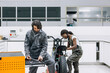 © Oscar Gimbal/ADDICTIVE STOCK - Busy multiethnic male and female technicians in dirty workwear fixing motorcycle while using instruments from tool cabinet