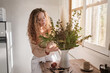 © Philippe Degroote/ADDICTIVE STOCK - Gentle female standing at table with bunch of fresh green plants in vase at home