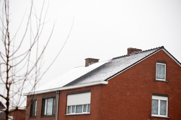 A portrait of two semi-detached buildings with white snow on their roofs during winter. The snow on one of the houses is already melting due to a badly isolated roof.