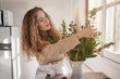 © Philippe Degroote/ADDICTIVE STOCK - Gentle female standing at table with bunch of fresh green plants in vase at home