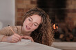 © Philippe Degroote/ADDICTIVE STOCK - Content female in domestic wear sitting in cozy house against fireplace and writing in diary