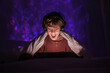 © Philippe Degroote/ADDICTIVE STOCK - Excited teenage boy in headphones sitting on bed in dark room with glowing lights while smiling and watching video on tablet