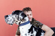 © Sergio Victor Vega/ADDICTIVE STOCK - Side view of happy young unshaven male in casual clothes and adorable obedient Harlequin Great Dane dog hugging each other against red background