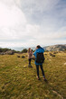 © Ruben Soto/ADDICTIVE STOCK - Unrecognizable male trekker taking photo of female partner on camera while standing on lawn against mount under cloudy sky