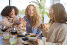Group Of Cheerful Multiracial Young Women Having Fun While Eating Traditional Asian Ramen During Dinner In Restaurant