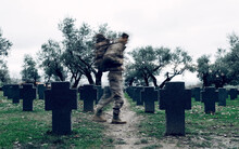 Side View Anonymous Soldier In Camouflage Carrying Warrior Backpack Walking In Spacious Military Cemetery