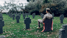 Back View Full Body Of Soldier In Uniform Sitting On Chair With American Flag While Mourning Death Of Warriors At Graveyard