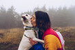 © Ruben Soto/ADDICTIVE STOCK - Side view of loving female owner kissing adorable white dog during stroll in nature on foggy day