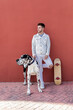 © Sergio Victor Vega/ADDICTIVE STOCK - Full body of trendy young male in casual clothes with skateboard looking away while standing on street with adorable Harlequin Great Dane dog