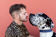 © Sergio Victor Vega/ADDICTIVE STOCK - Side view of happy young unshaven male in casual clothes and adorable obedient Harlequin Great Dane dog hugging each other against red background