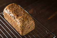 From Above Of Freshly Baked Loaf Of Sourdough Bread With Crispy Crust And Grains Placed On Metal Grid On Wooden Table