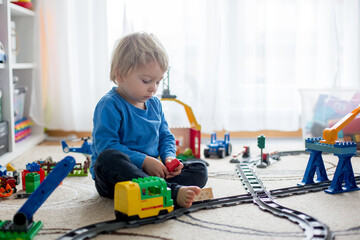 Wall Mural - Adorable little boy playing with colorful plastic construction blocks at home, sitting on the floor, train going on railroad