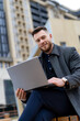 © Vadim - Happy smiling businessman in coat working and watching with laptop on modern wide street.