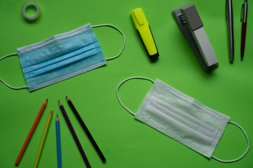 Mouth cover on a green surface. Along with them there are pencils and school supplies
