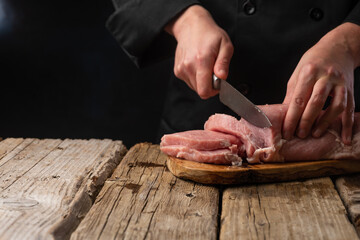 Wall Mural - Chef cuts fresh pork fillet. On a dark background. Banner, sale and preparation of meat, recipes and menus.