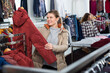 Portrait of cheerful female customer choosing new coat in showroom