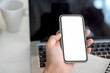 © amnaj - Image of a businessman holding smartphone a blank screen, laptop placed on an office table. Mock up.