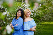 © Elena  - Two young women brunette and blonde plus size in a blooming garden enjoy nature and have fun. Apple orchard in spring.