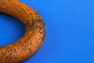 a half of fresh baked bagel with poppy seeds on the blue background - close up with copy space, food photo and concept