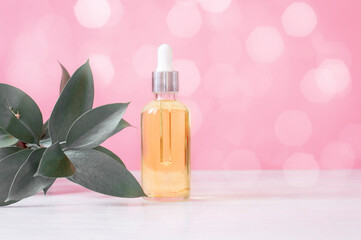 Cosmetic oil on a pink background with bokeh and a sprig of greenery. The concept of skin care.