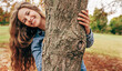 © iuricazac - Positive young woman smiling, wearing a blue denim shirt embraces a tree, posing on nature background. Candid portrait of a happy female enjoying the time in the park. Mental health concept