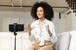 © Vadim Pastuh - Smiling female African American blogger influencer sitting at phone on stabilizer, recording new video for subscribers or streaming educational lecture, sharing knowledge live online at home office