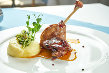 Wall Mural - Duck leg confit with sweet sauce garnished with mashed potatoes in a white plate on a blue tablecloth