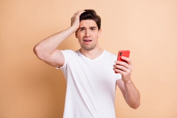 Photo of confused young guy hold arm on head sullen face stupor bad news isolated on beige color background