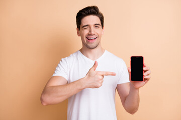 portrait of positive handsome person eye wink direct finger empty space display isolated on beige co