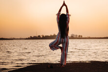 Young Indian Woman Standing Near Lake Doing Yoga, Meditation During Time Of Sunrise. Concept Of Healthy Lifestyle
