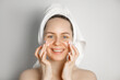 © piksik - Skin care concept.Young smiling female in towel applying face cream. Taking care of young skin concept.Problem skin